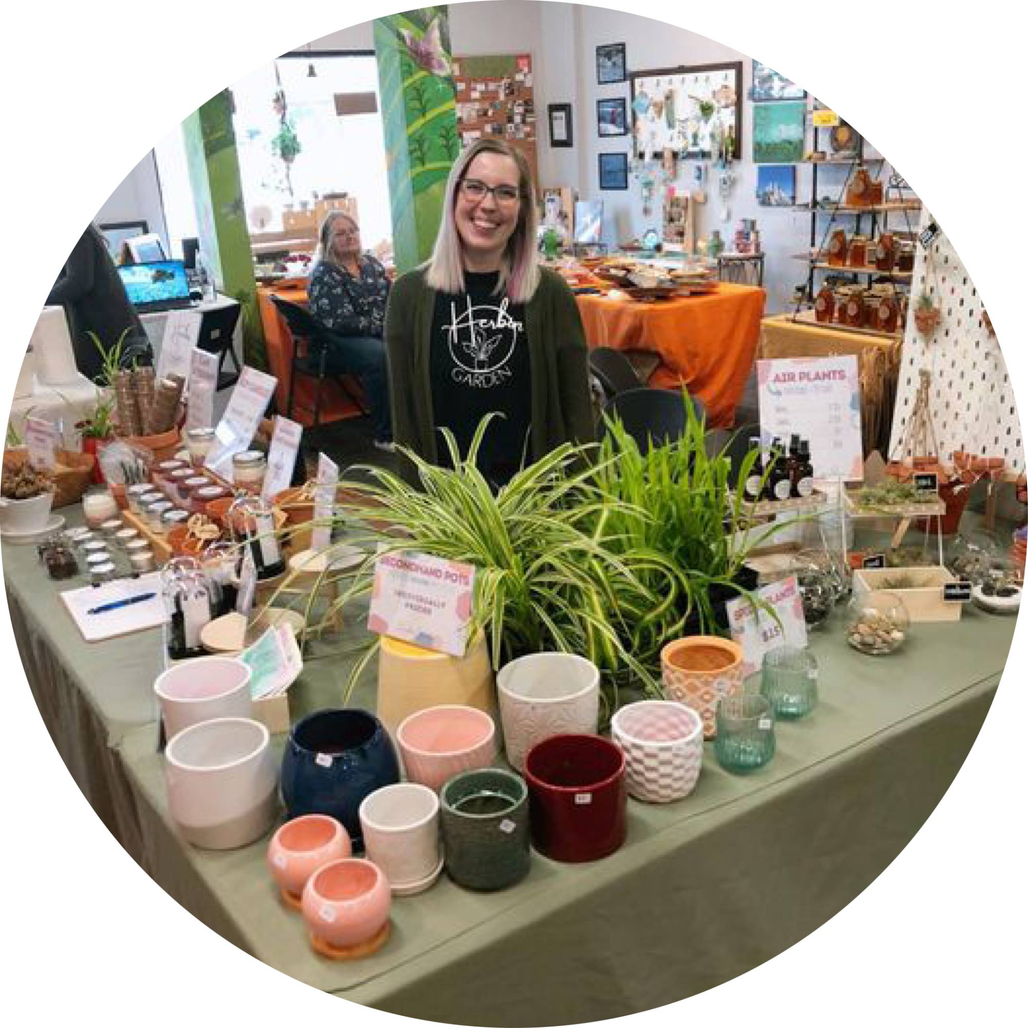 Owner of Herbin Garden standing behind their booth of assorted plants and ceramic pots